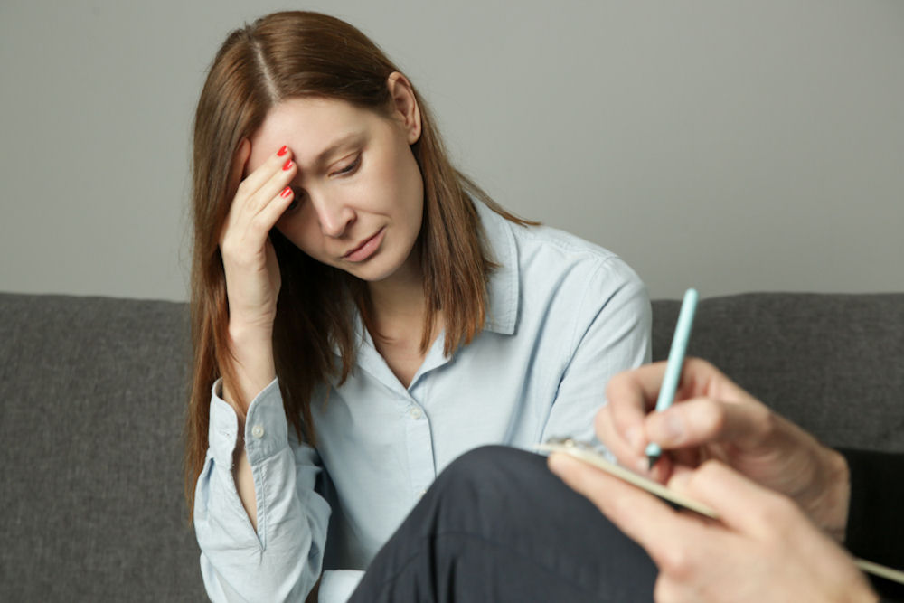 Woman holding head while speaking with doctor about meth addiction.