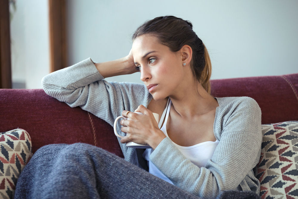 Woman with coffee cup in hand looking out the window and thinking about captagon.