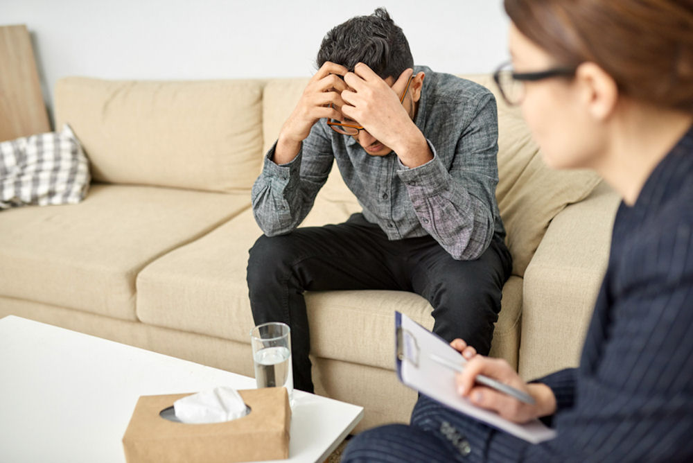 Man leaning over and holding head while discussing trauma.
