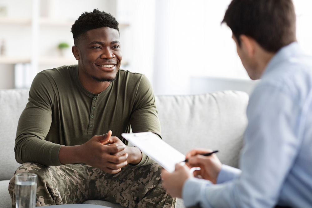 Combat veteran speaking with therapist about insurance coverage for addiction treatment.